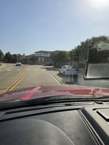 Driver-eye view toward bright afternoon sun with a privacy-redacted vehicle and a concrete bump-out ahead